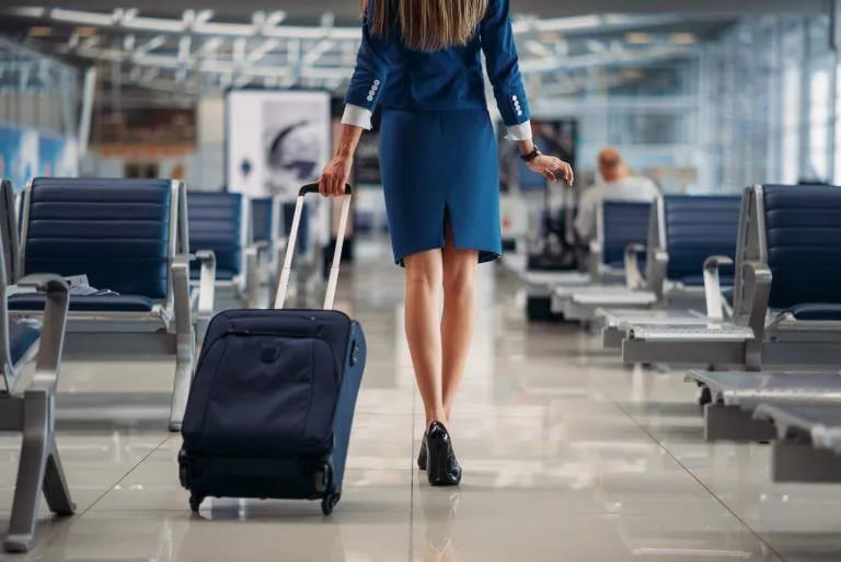 Corporate flight attendant confidently walks through airport, suitcase in tow, exuding professionalism for her next flight